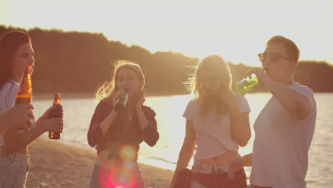 Five-teenagers-celebrate-a-birthday-on-the-beach-party-with-beer-and-good-mood.-They-drink-beer-and-dance-in-the-hot-evening.-This-is-carefree-party-at-sunset.